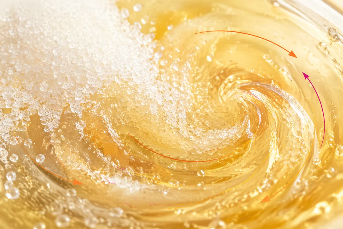 Granulated sugar dissolving into a clear golden syrup in a mixing vessel